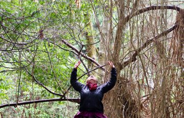 Celeste Snowber raises her arms to the skies; trees in background